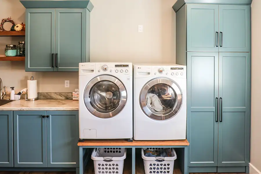Mud room, Laundry Room, with custom teal cabinetry and blond wood shelving, washer and dryer elevated with laundry basket storage underneath | Eureka, IL